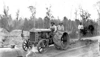 Old tractor pulls inmate standing on platform to level dirt on road