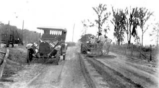 Old car and convicts working on dirt road