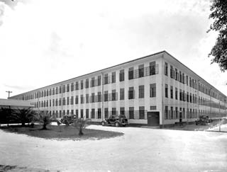 Three story, white building with barred windows and 1930 automobiles parked in front.