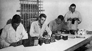 Four men at large table working on billfolds, purses and other objects.