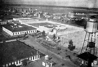 Aerial view shows 4 large buildings, a large tower and many small houses in the distance.