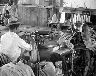 Inmates sitting a sewing machines with large spools of thread.