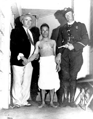 Photo of Giuseppe Zangara in custody after his unsuccessful attempt on President Roosevelt’s life, standing between two officers.