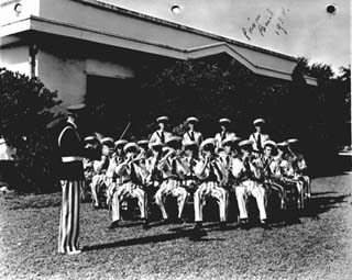 Inmates in prison uniforms sitting in chairs with musical instruments.