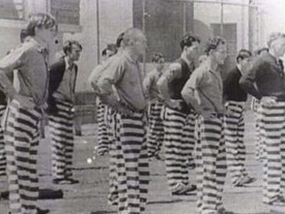 Inmates standing in line with their hands on their waists.