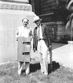 Two men holding a wooden leg restraint and a heavy chain.