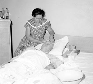 Dobbs laying onside in hospital bed with nurse sitting on left.