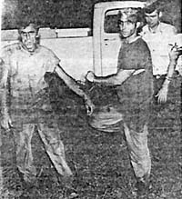 Two men standing in front of truck.  Officer is behind and to the left.