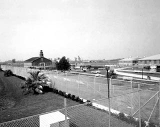 Small building with steeple, corners of other buildings and lots of fence.