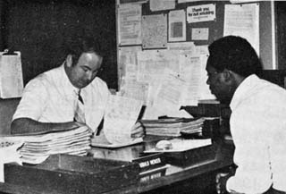 Officer behind desk looking a papers and offender sitting in chair facing desk