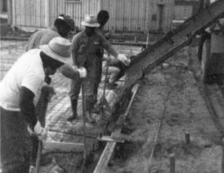 Inmates working on a building foundation with school building in background