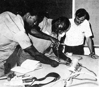 Instructor and two inmates leaning over table filled with electronic components