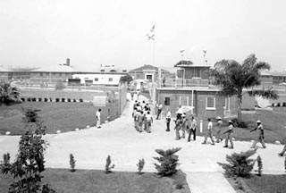 Inmates marching into fenced area with many buildings.