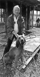 Gray-haired man standing behind a bloodhound.