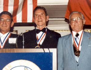 Three men standing behind podium with flag in background.