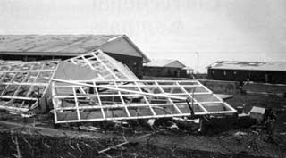 Wood wall frames without siding and buildings with missing roof shingles in the background.