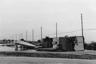 Row of shattered mobile homes, large puddles of water and broken power lines.